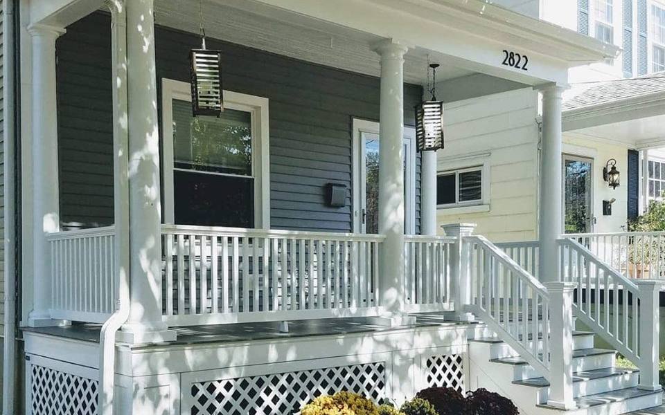 A white-painted front porch with turned columns and a spindle rail on a Cincinnati house, with autumn plants along the step.