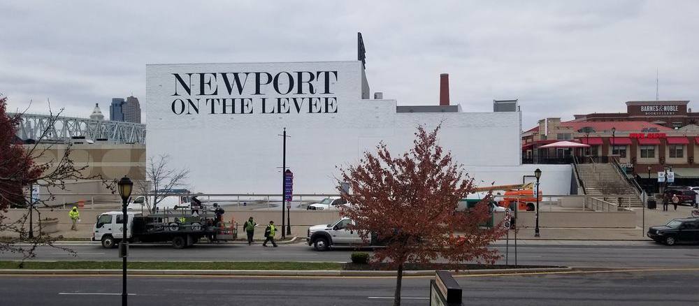 Large hand-painted lettering reading Newport on the Levee across a tall white building wall.